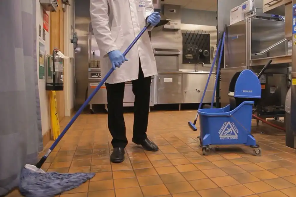 Janitor white white coat and blue gloves mopping commercial kitchen area