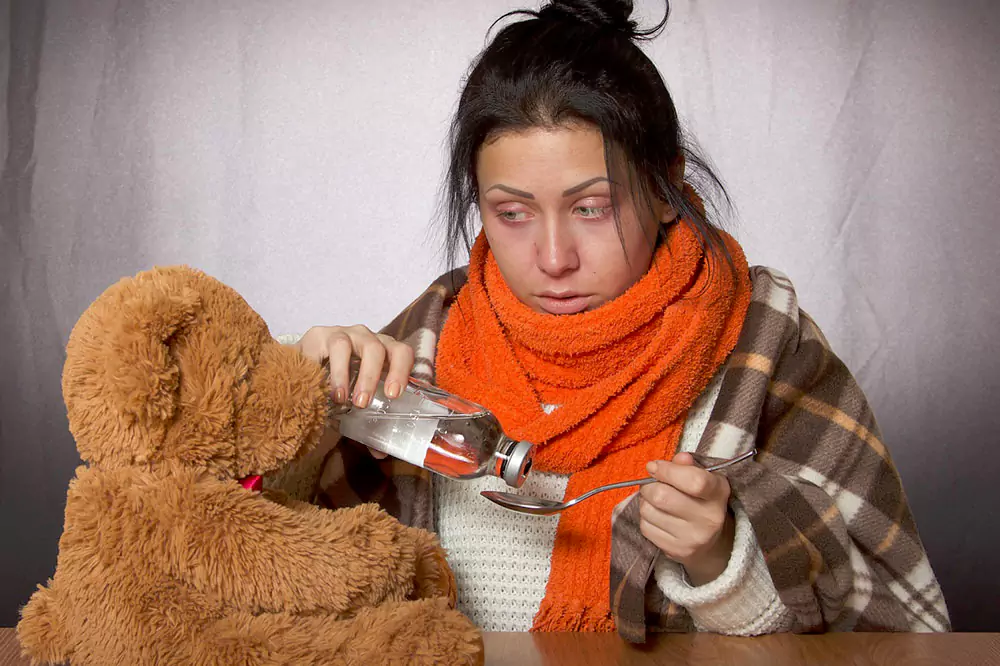 Sick woman taking cold medicine wrapped in a blanket