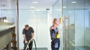 Male and female janitors vacuuming floor and wiping windows in commercial office