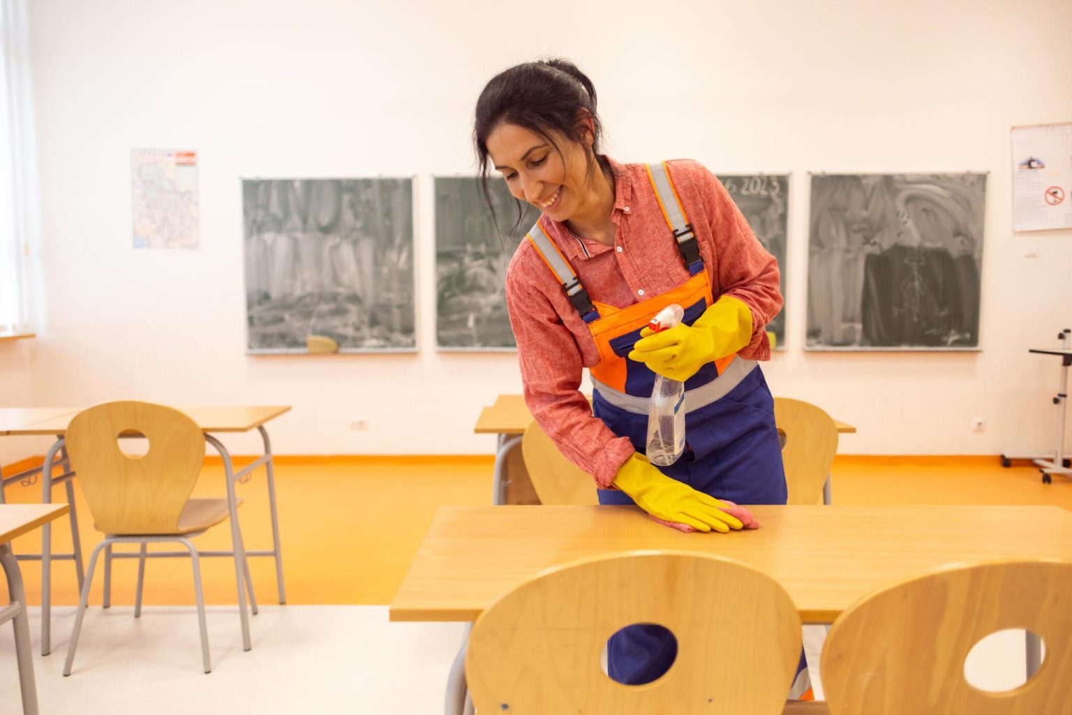 Woman janitor cleaning tables in k-12 classroom