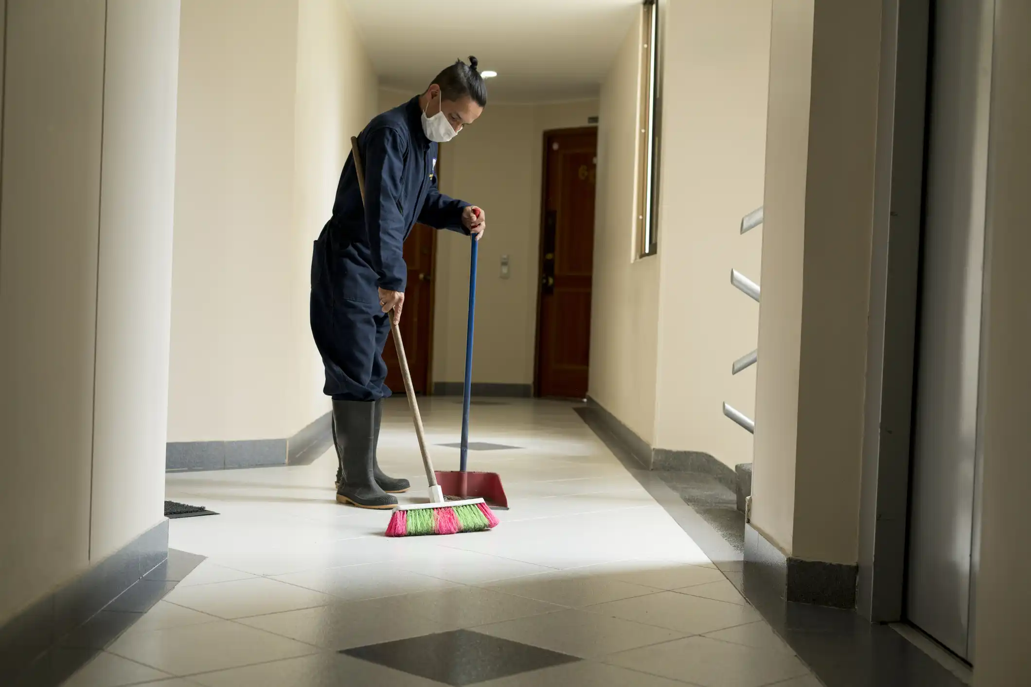 Janitor sweeping floor and placing debrit in dustpan.