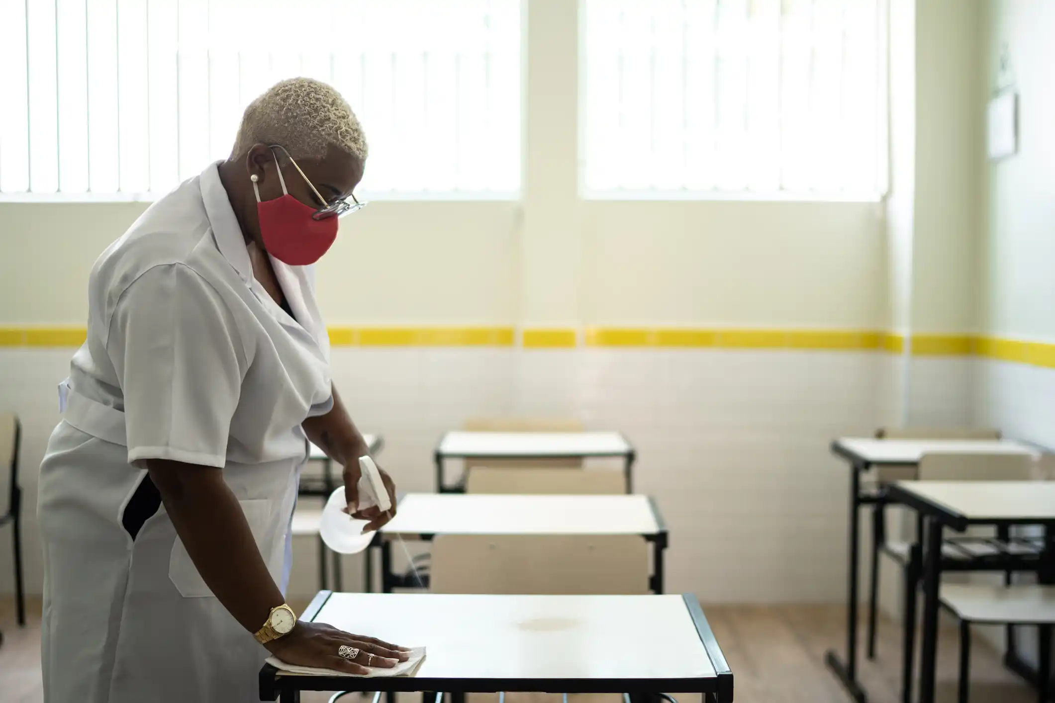 Woman janitor cleaning tables in education classroom