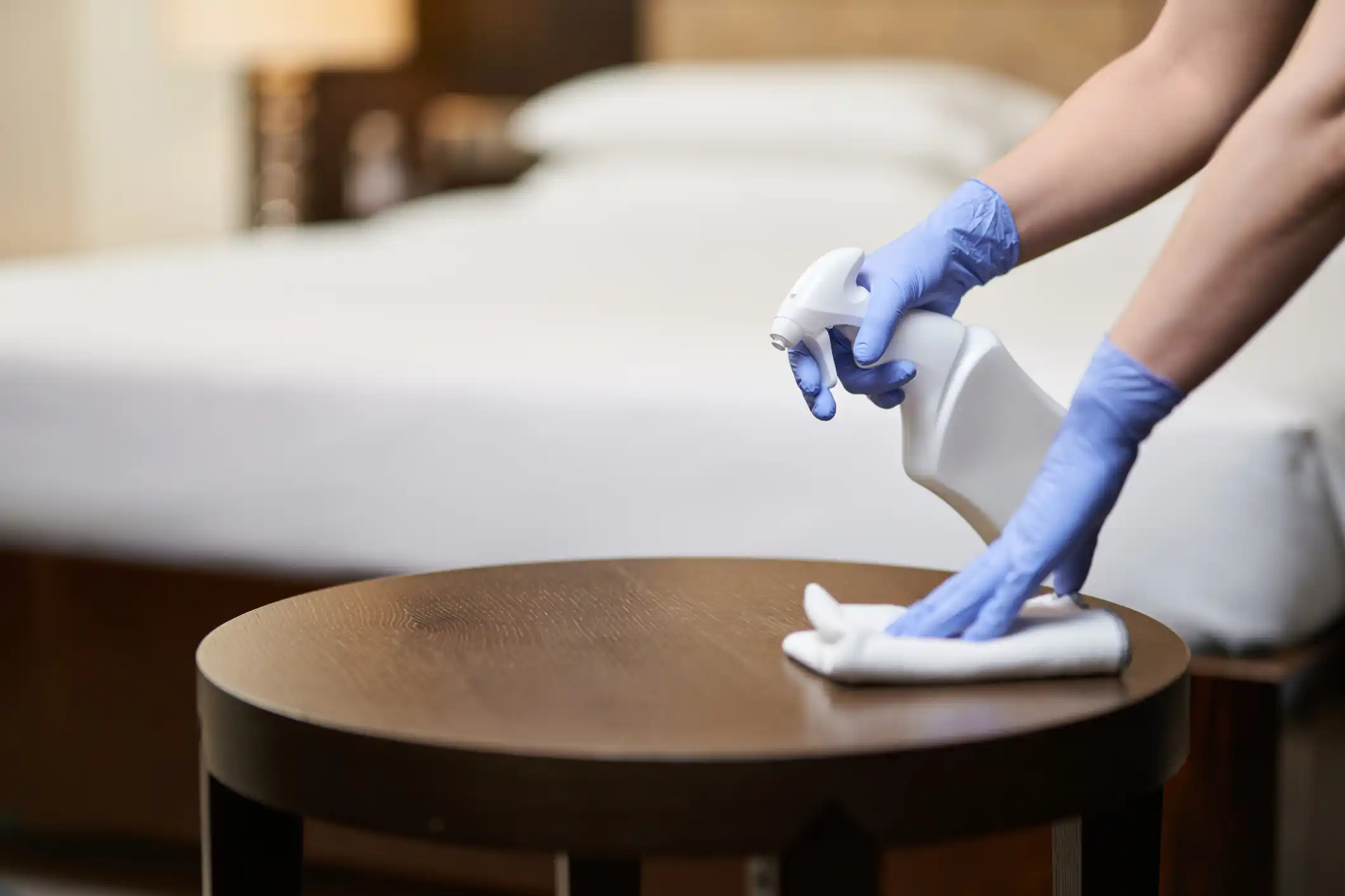 Woman cleaning table with spray and cloth and gloves on