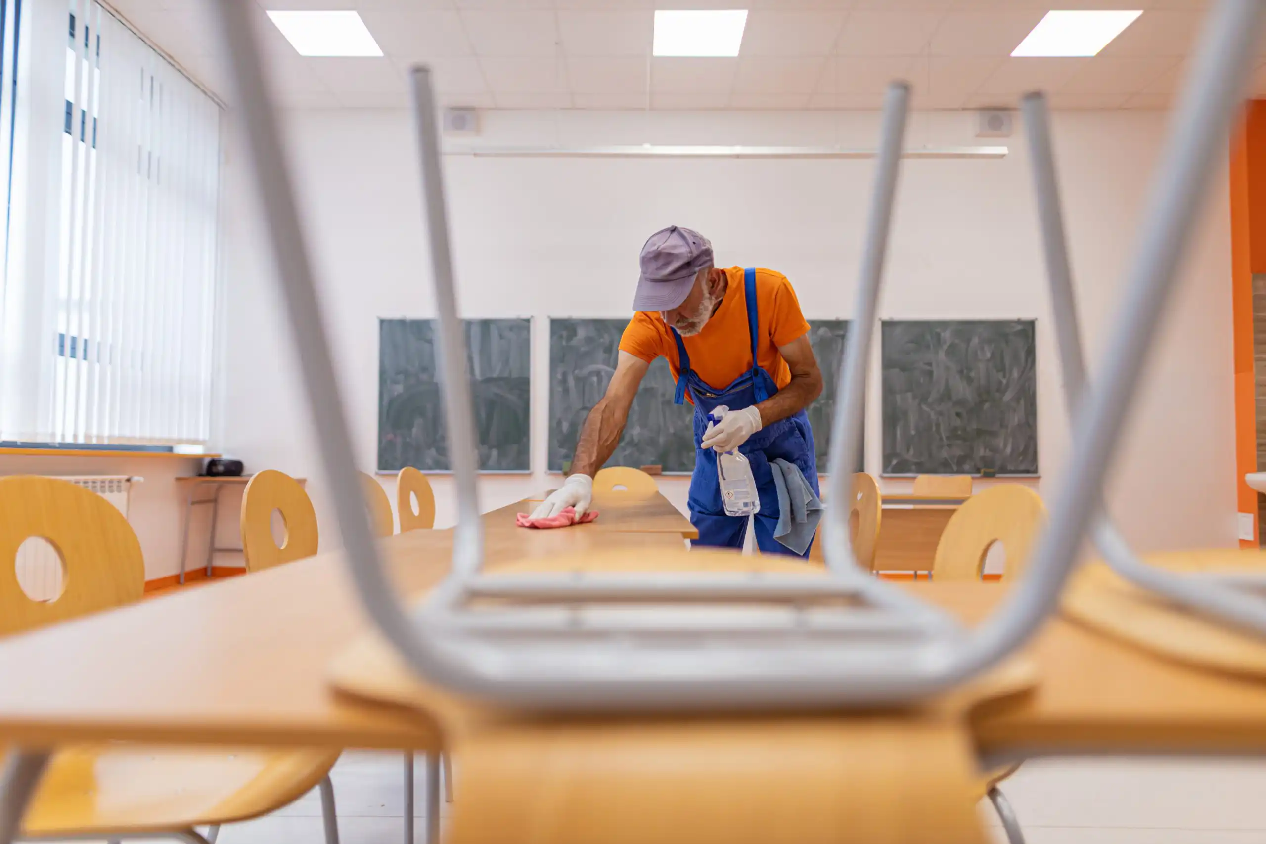 Janitor cleaning tables turned upside down on desks.