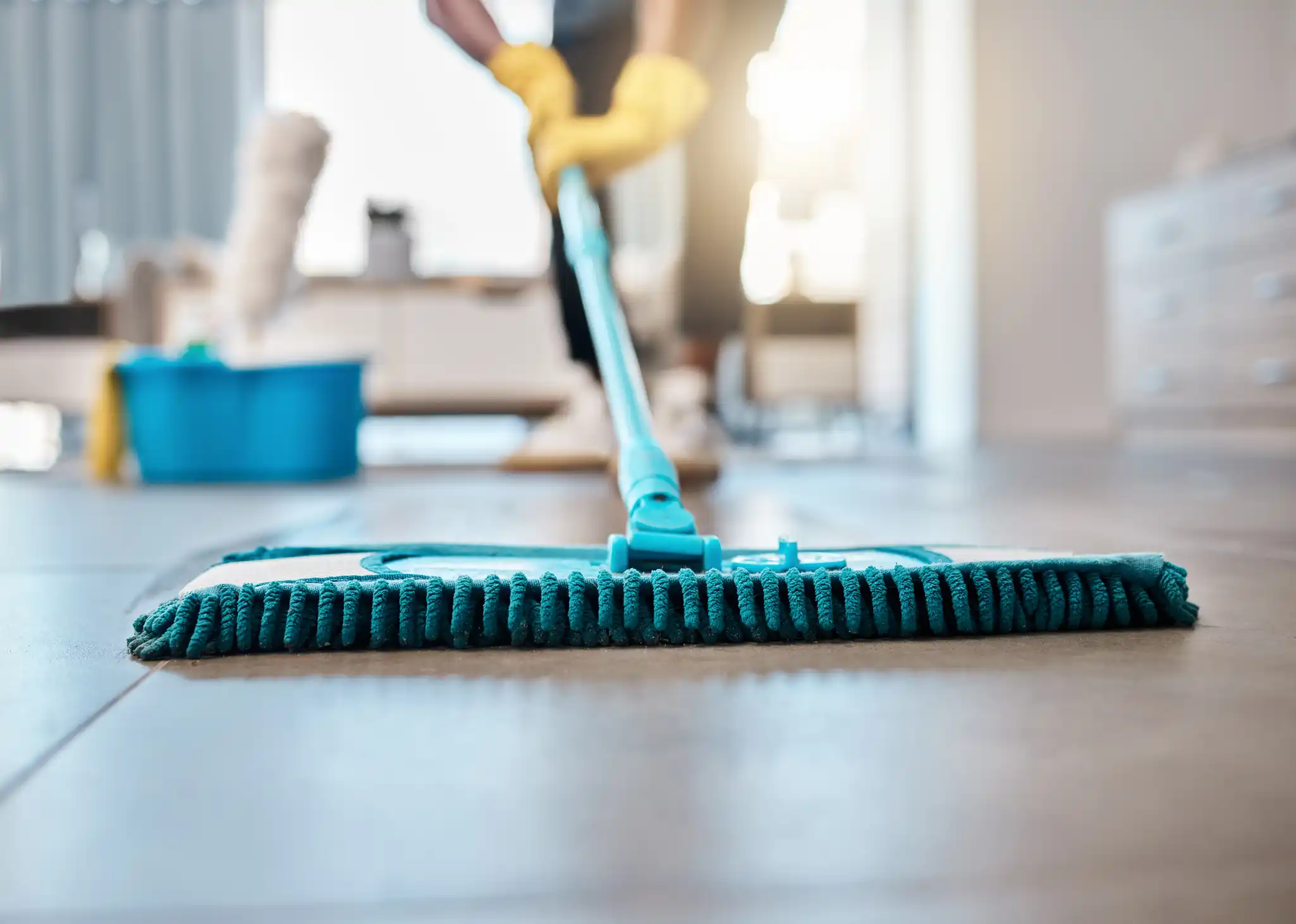 Cleaner with yellow gloves on sweeping floor with big broom in hospital