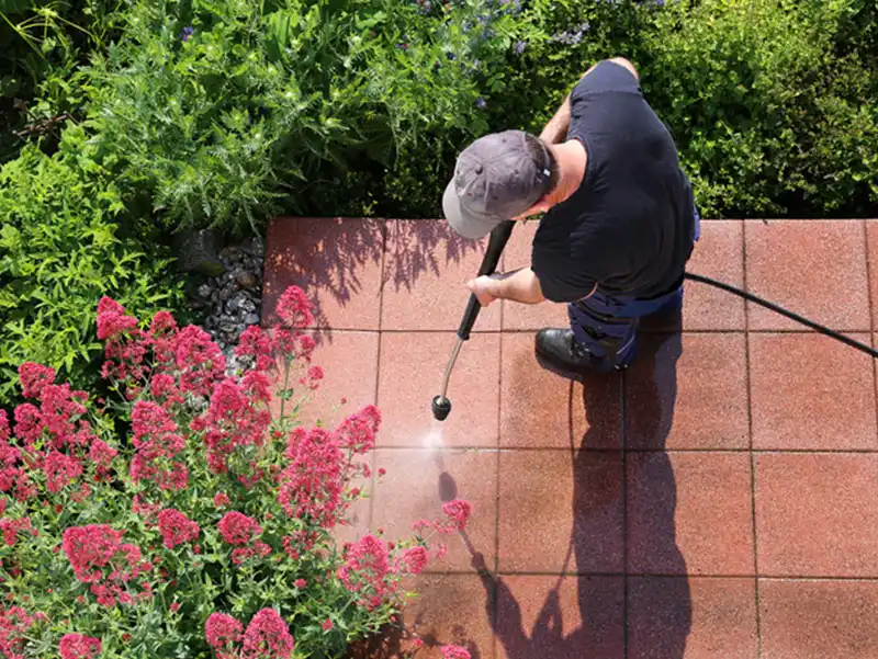 Maintenance man power washing brick walkway with pressure washer