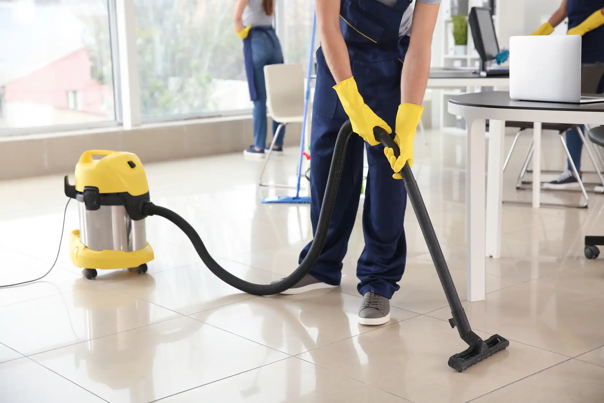 Janitor with long yellow gloves vacuuming tile floor.