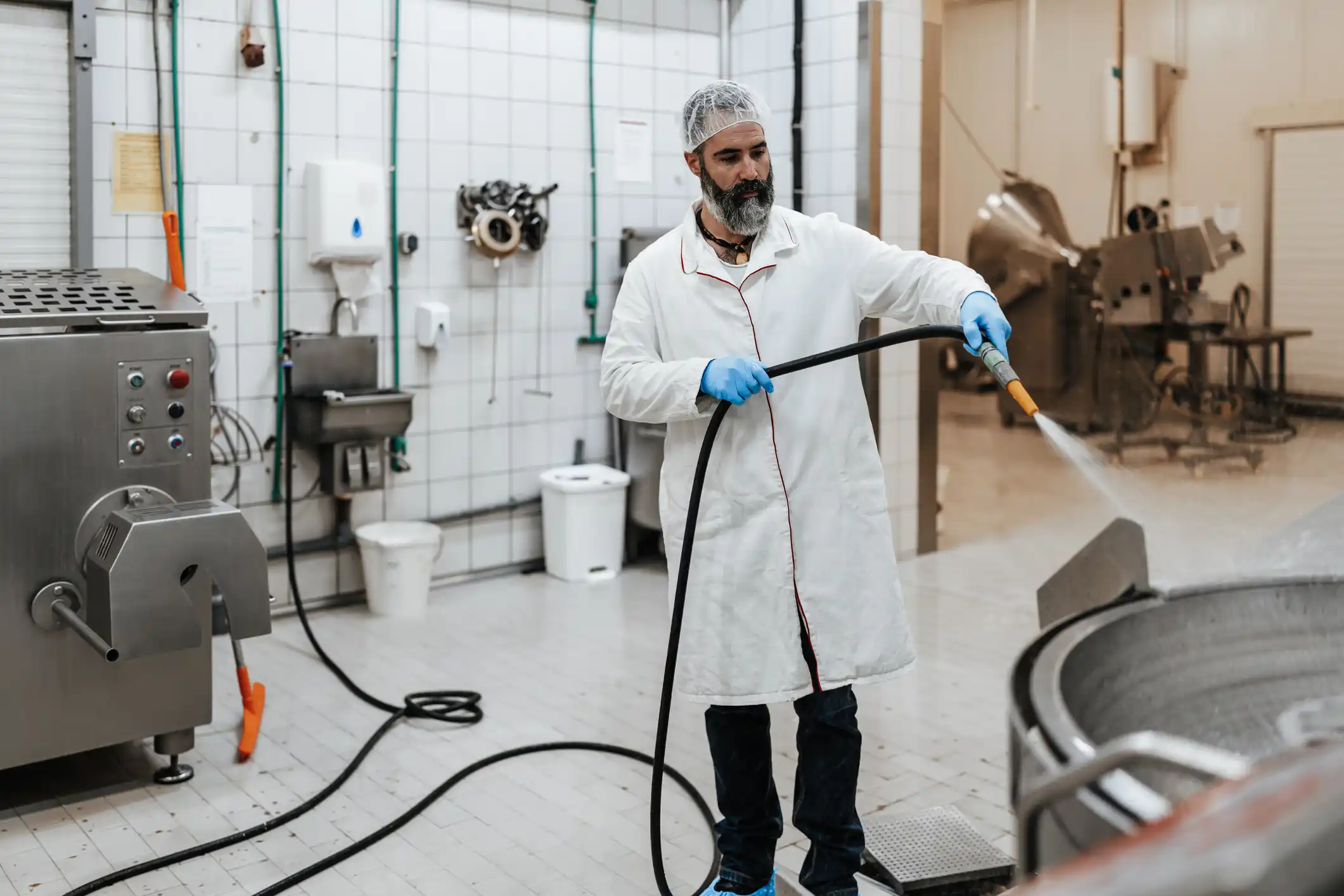Factory worker with white coat, blue gloves and hairnet on cleaning food container