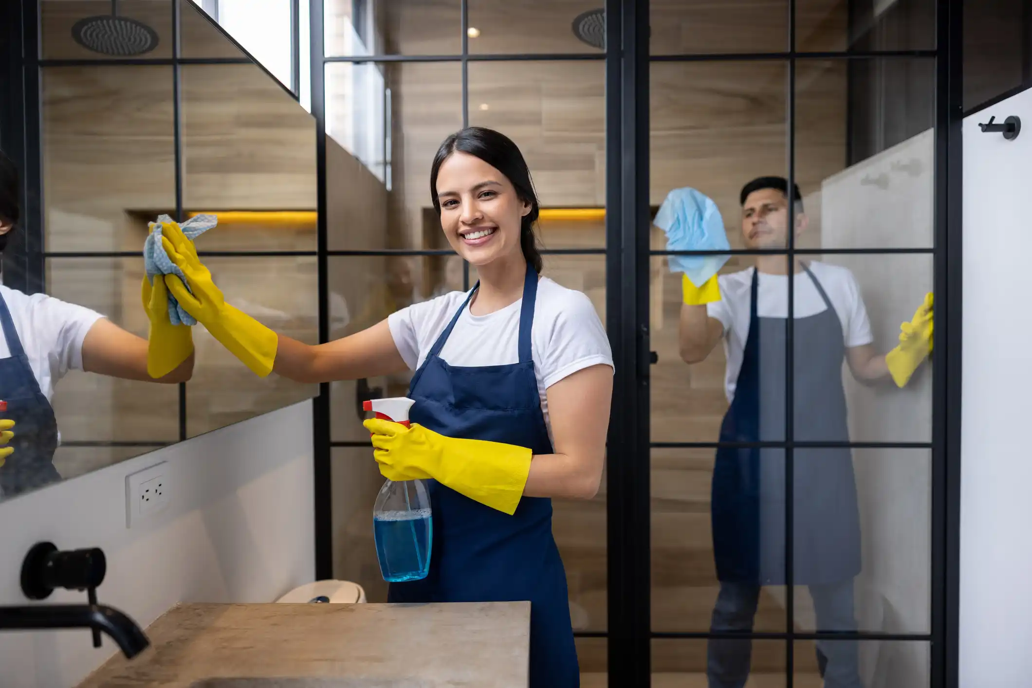 Woman cleaner with long yellow gloves on cleaning glass windows in home office