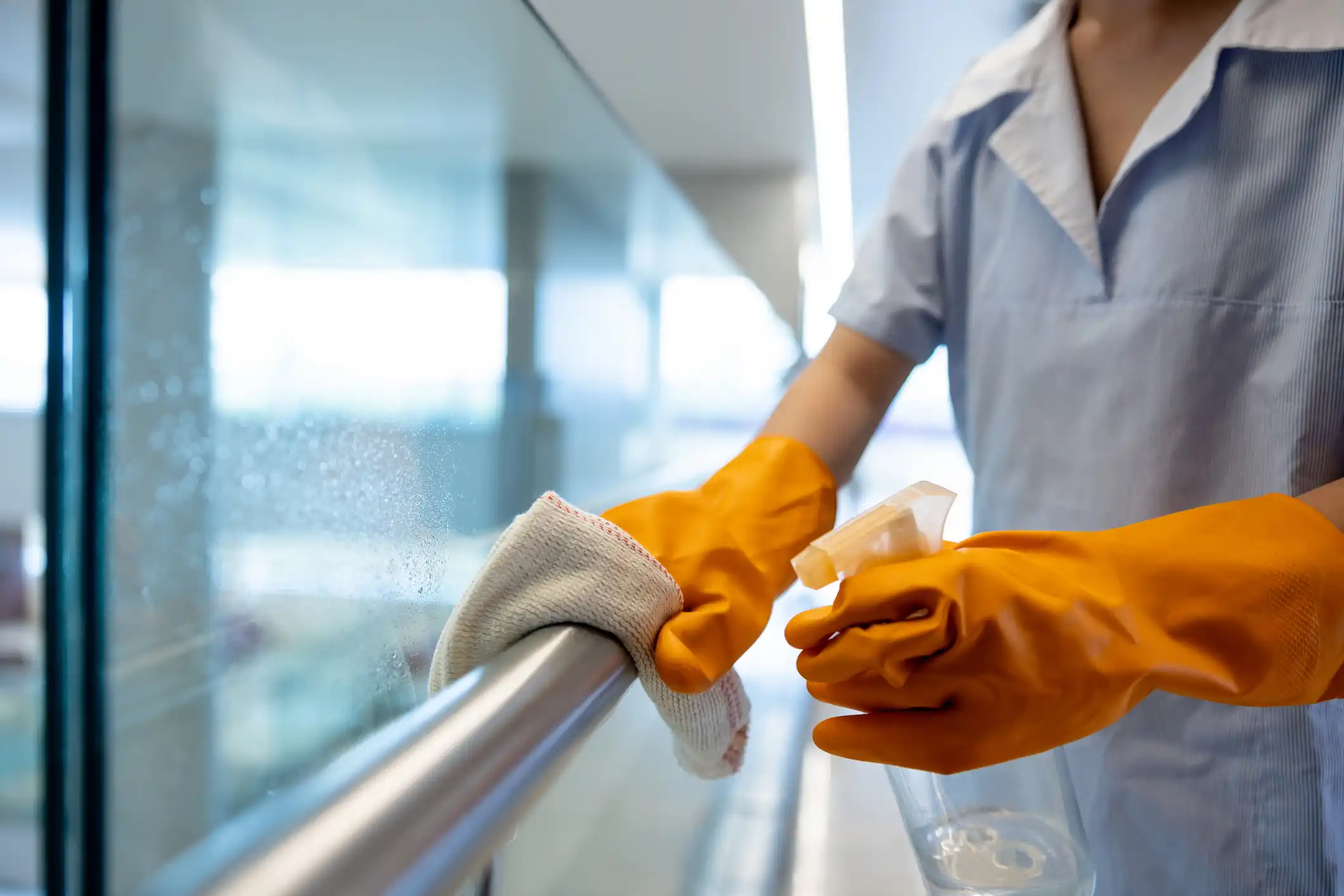 Janitor wiping railing with orange gloves and cloth