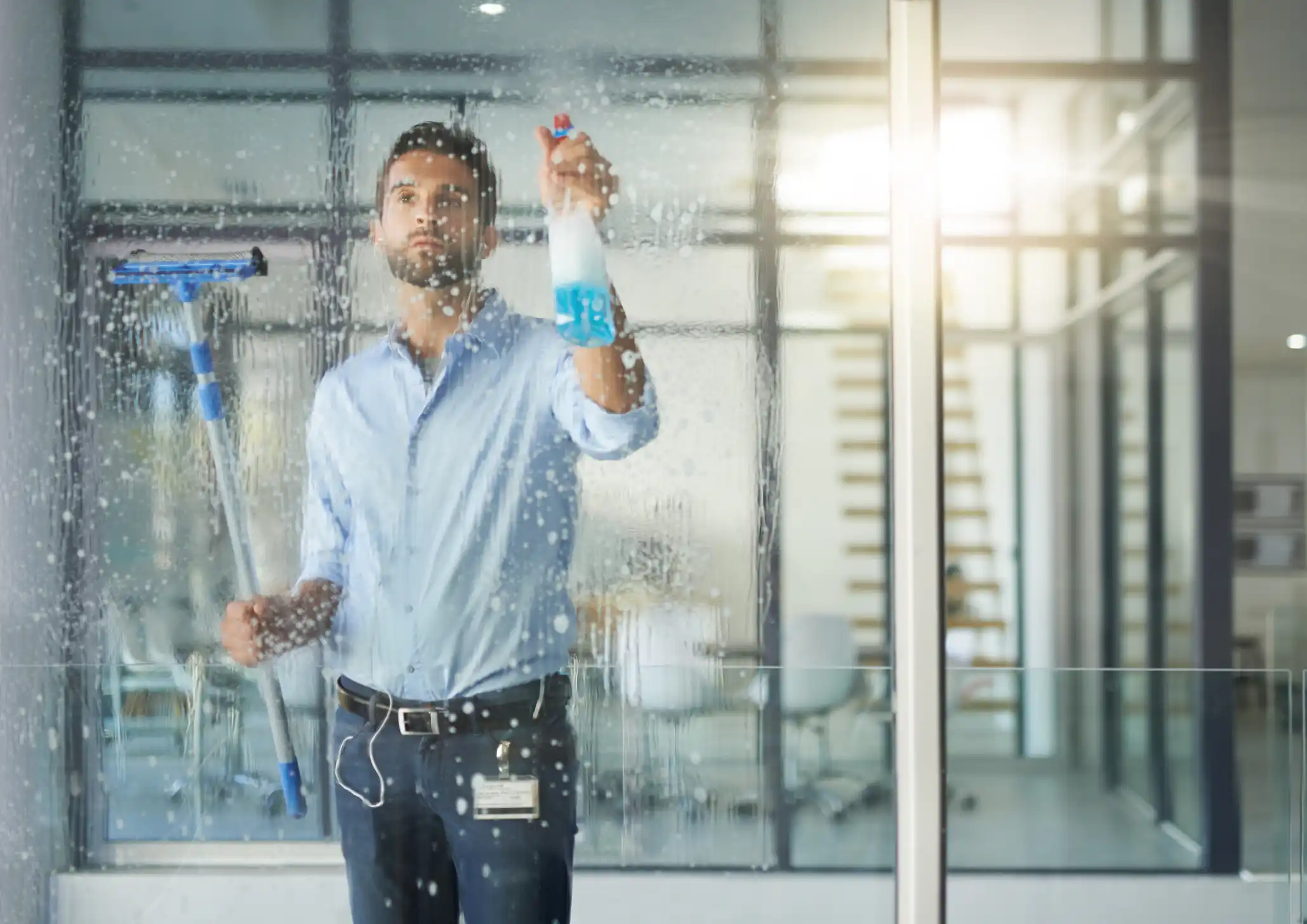 Man cleaning glass windows in office with spray and wiper in hand