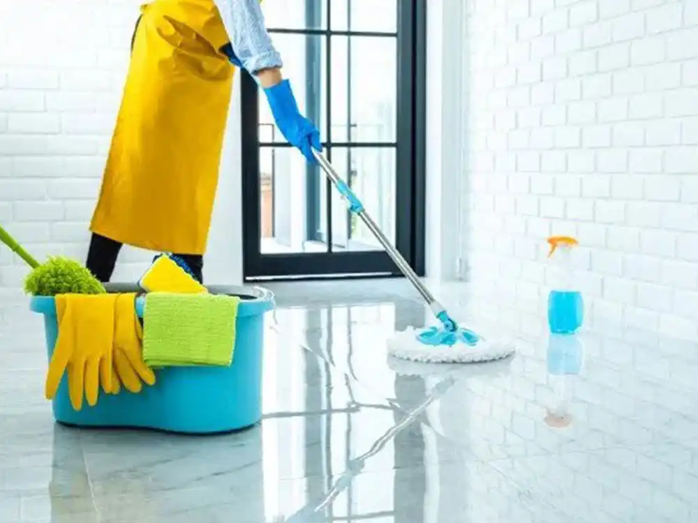 Women cleaner in apron and blue gloves mopping floor with sliding glass door in background